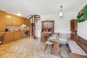 Een keuken met houten kastjes, een spiltrap, een eettafel met stoelen en een groen wandplankje.