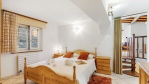 Een slaapkamer met een houten bed, nachtkastjes, een gordijn en een trap.