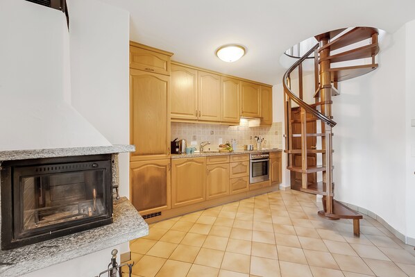 Eine Küche mit Holzausstattung, einem eingebauten Ofen, einer Arbeitsplatte aus Granit und einer Wendeltreppe.