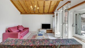 Een woonkamer met een houten plafond, een roze bank, een televisie en een groot raam.