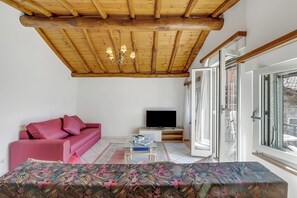 Ein Wohnzimmer mit Holzboden, einem rosafarbenen Sofa, einem Fernseher und einem großen Fenster.