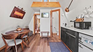 Eine kompakte Küche mit einem Holzespeise Tisch, Stühlen und einer kleinen Bank. Ein Fernseher ist an der Wand befestigt, und über der Küche befindet sich eine Holz-Galerie.