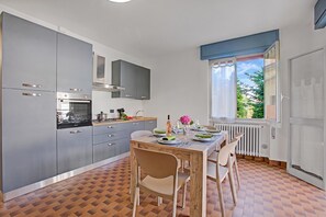 A modern kitchen with grey cabinets, a built-in oven, and a dining area with a table set for two. - Diana & Mark family house, Vobarno, Italy (Vobarno)