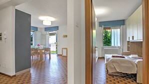 A bedroom with a bed, a window with curtains, and a radiator. There is a dining area with a table and chairs in the background. - Diana & Mark family house, Vobarno, Italy (Vobarno)