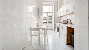 Una cucina stretta con mobili bianchi, una lavatrice e una finestra con vista sugli edifici.