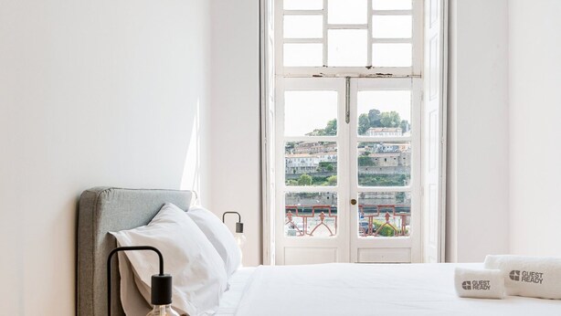 Una camera d'albergo con un letto, una lampada da comodino e vista sui palazzi attraverso una finestra.