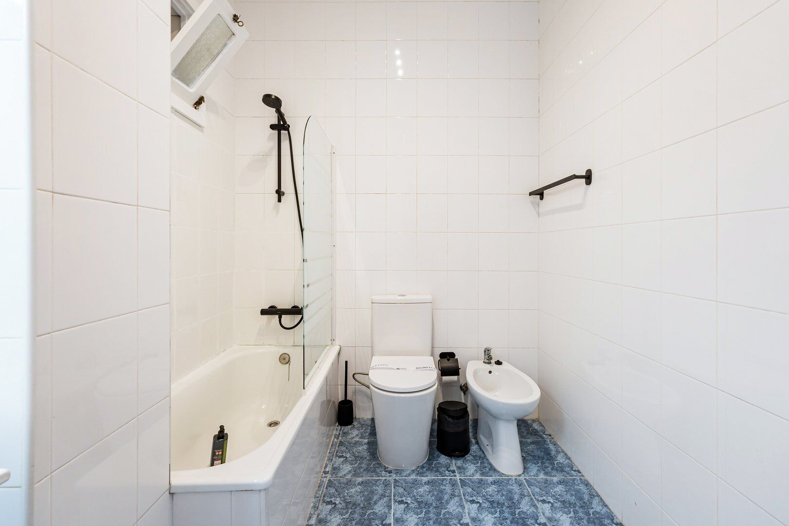 A small bathroom with white tiles, a bathtub, a toilet, and a bidet.