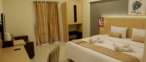 Una habitación de hotel con cama, escritorio, silla, armario y cortina.