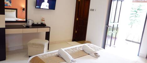 A hotel room with a bed, a desk, a television, and a door leading to a balcony.