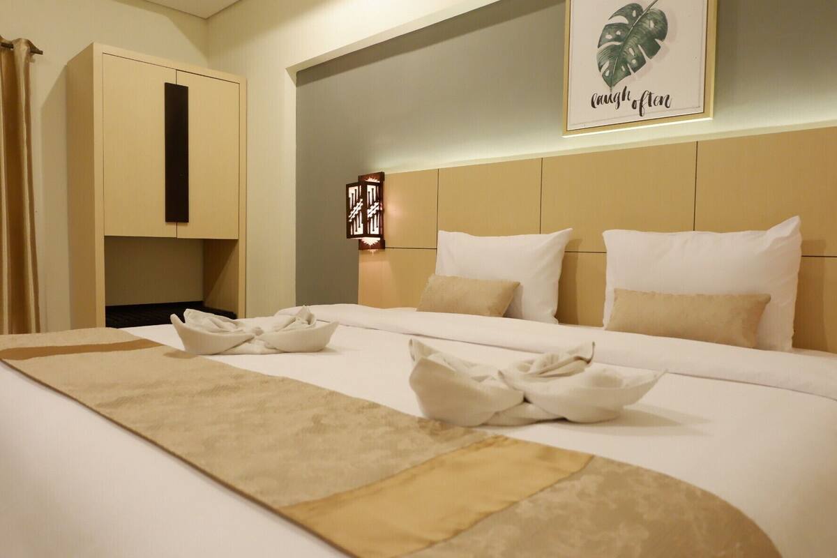 A hotel room with a large bed, a headboard with a light fixture, and a wall-mounted artwork.