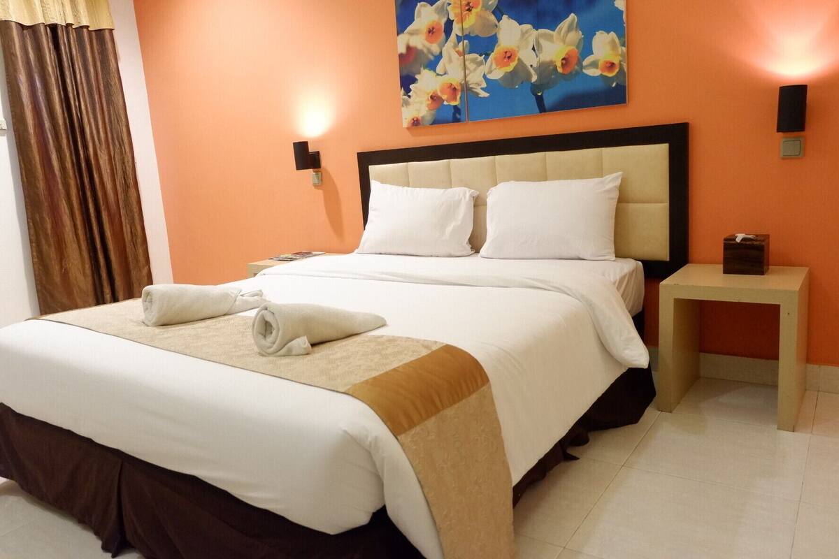 A hotel room with a large bed, white bedding, a beige throw, and a nightstand with a tissue box.