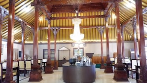Un vestíbulo amplio con un mostrador de recepción central, pilares de madera ornamentados y un alto techo con candelabro.
