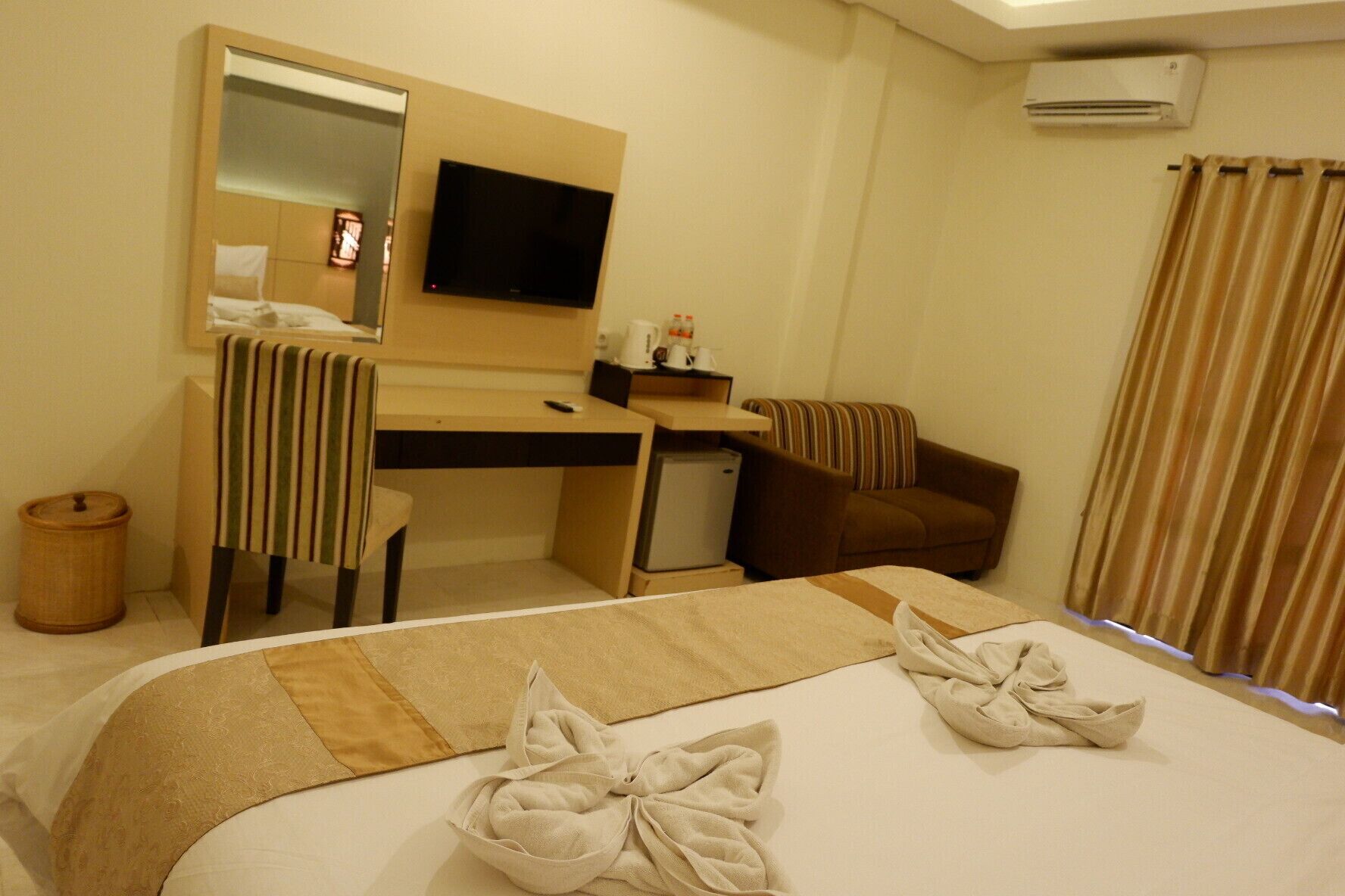 A hotel room with a bed, a desk, a chair, a television, and an air conditioning unit.