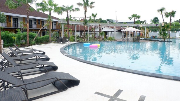 Zona de piscina con sillones de descanso, una alberca y palmeras.