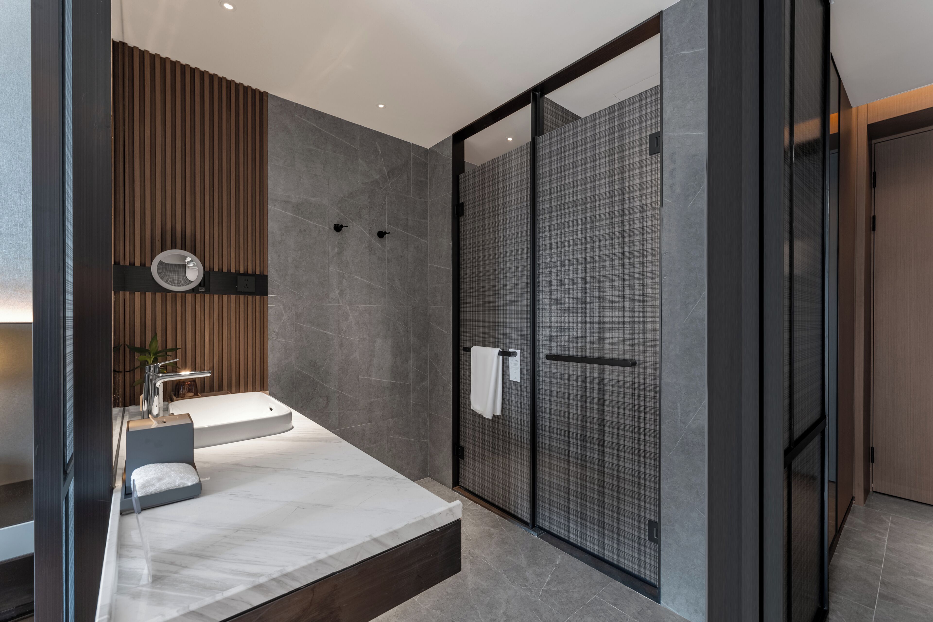 Un baño moderno con un espejo grande, dos lavamanos, una ducha con puerta de vidrio y un panel de pared de madera.