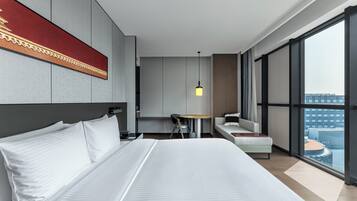 Una habitación de hotel moderna con una cama grande, un escritorio, una silla y un sofá. Hay un ventanal con vistas a la ciudad.