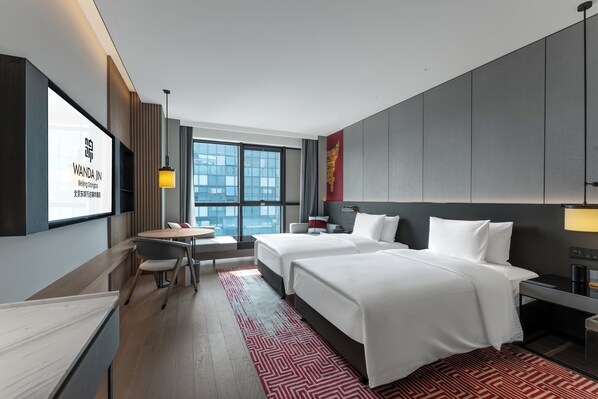 A hotel room with two beds, a desk, a chair, a TV, and a large window.