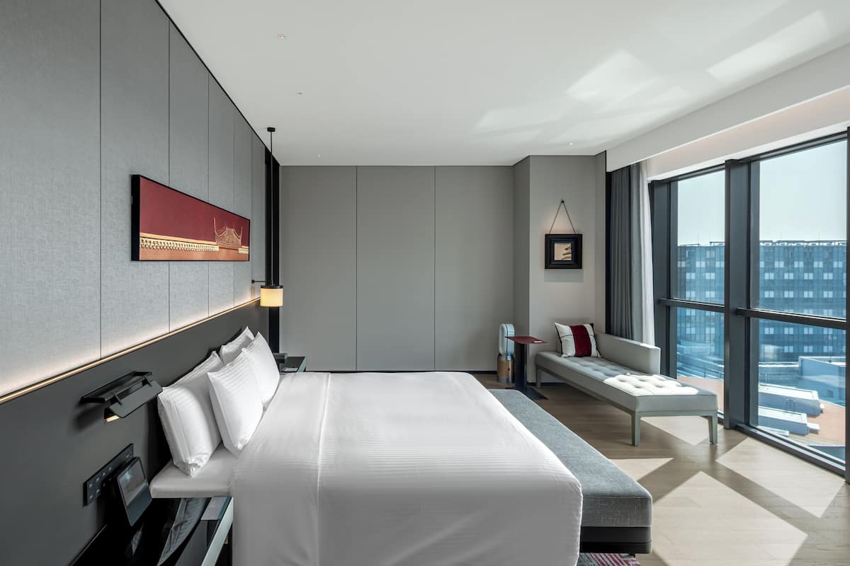 A modern hotel room with a large bed, a seating area, and a view of the city.