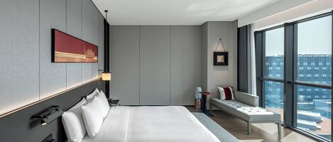 Una habitación de hotel moderna con una cama grande, un área de descanso y vistas a la ciudad.