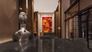 Un vestíbulo moderno con piso de mármol, una gran escultura abstracta y un mural tradicional rojo y dorado en la pared.