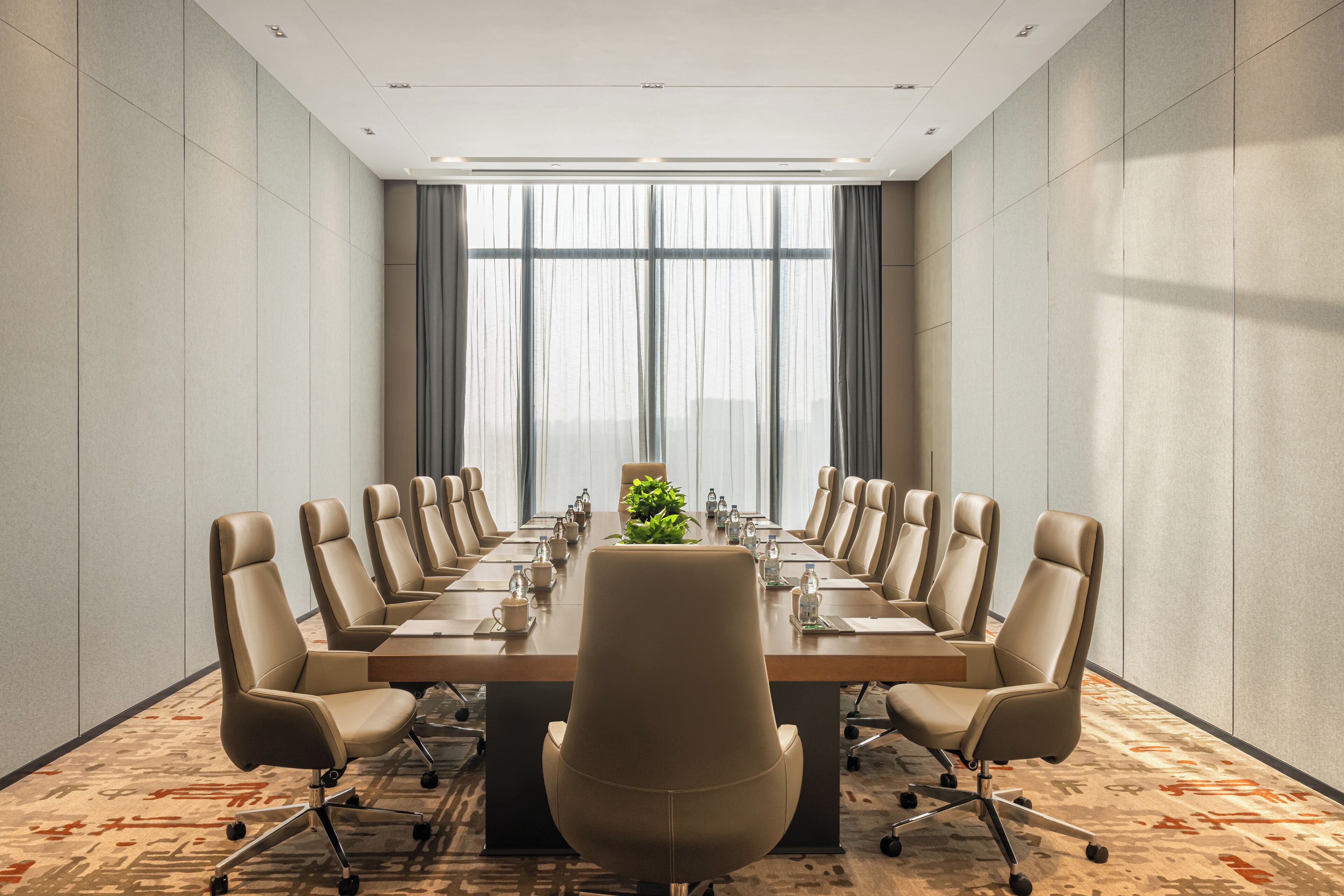 Uma sala de conferências com uma mesa comprida, várias cadeiras e um arranjo de plantas no centro.