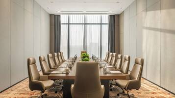Uma sala de conferências com uma mesa comprida, várias cadeiras e um arranjo de plantas no centro.