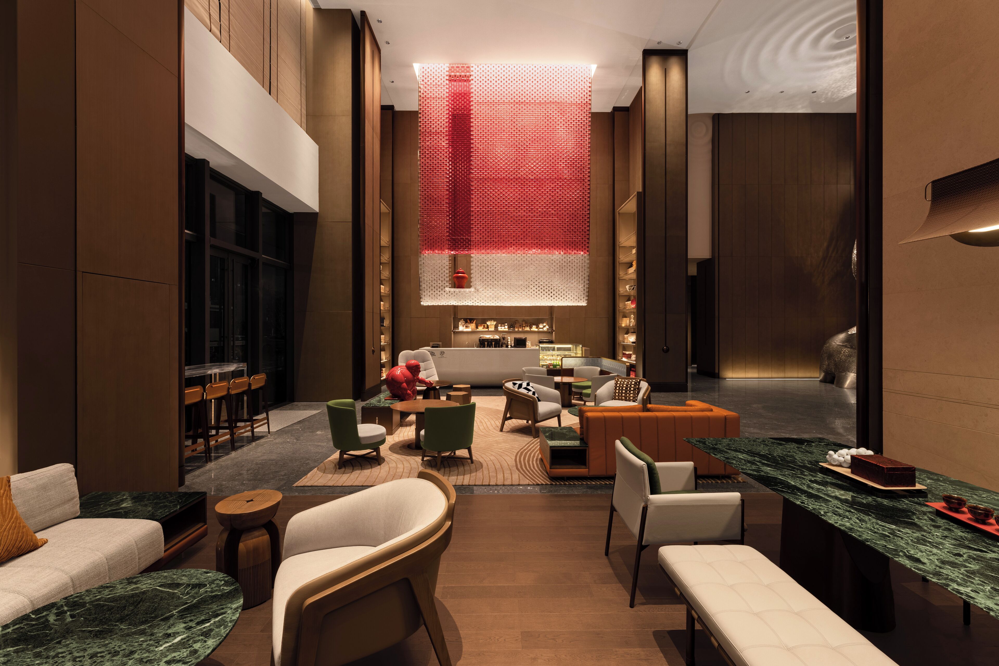 A modern hotel lobby with a seating area, a reception desk, and a large window with a red curtain.