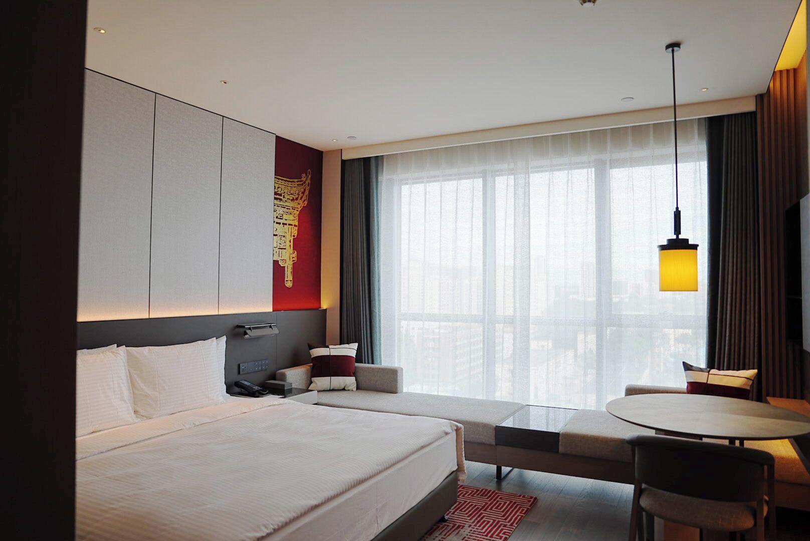 Moderni hotellihuone, jossa on suuri sänky, työpöytä ja tuoli. Huoneessa on ikkuna, jossa on verhot, ja ikkunasta avautuu näkymä kaupunkiin.