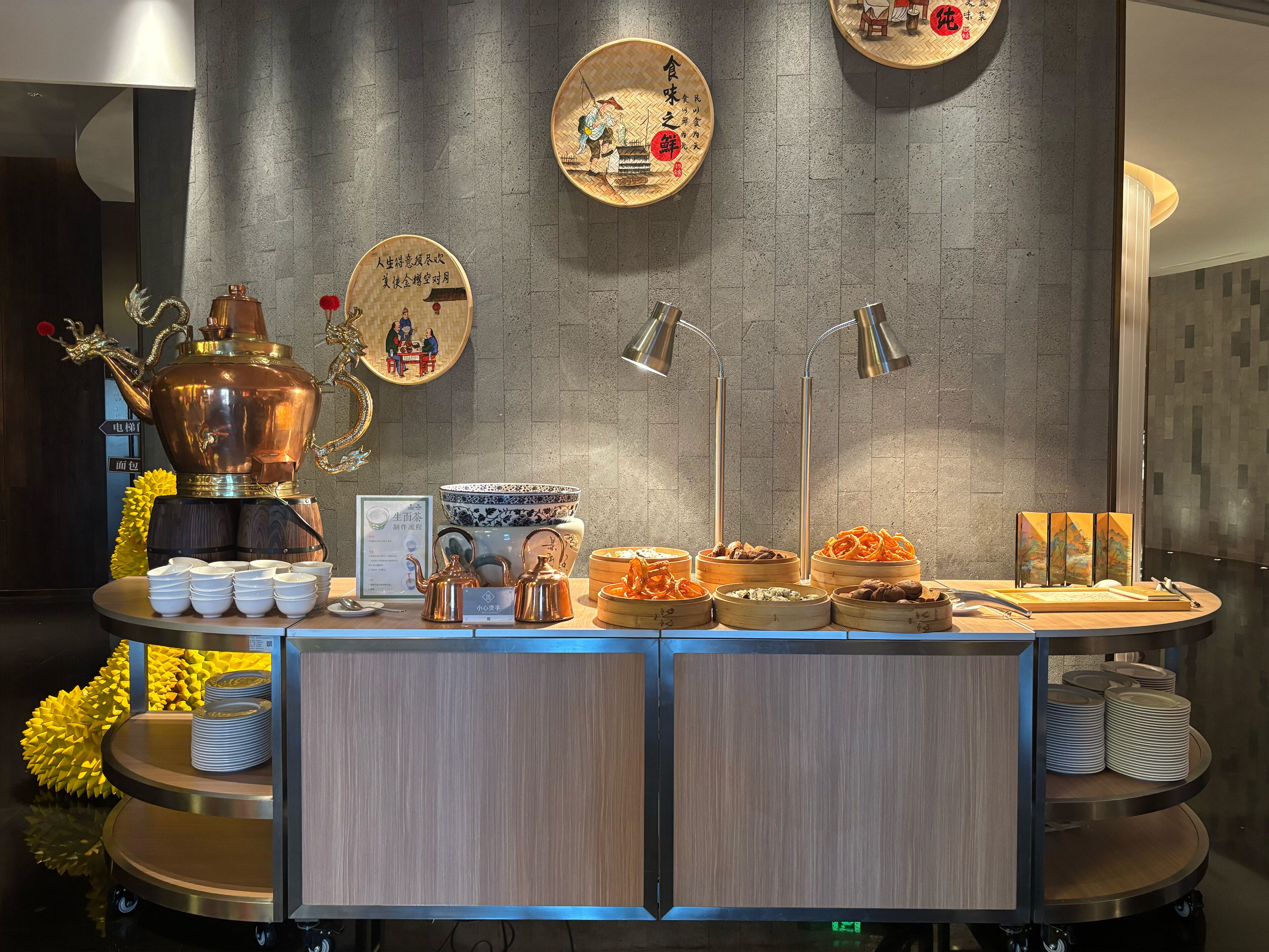 A buffet setup with various food items, a coffee station, and decorative plates on the wall.