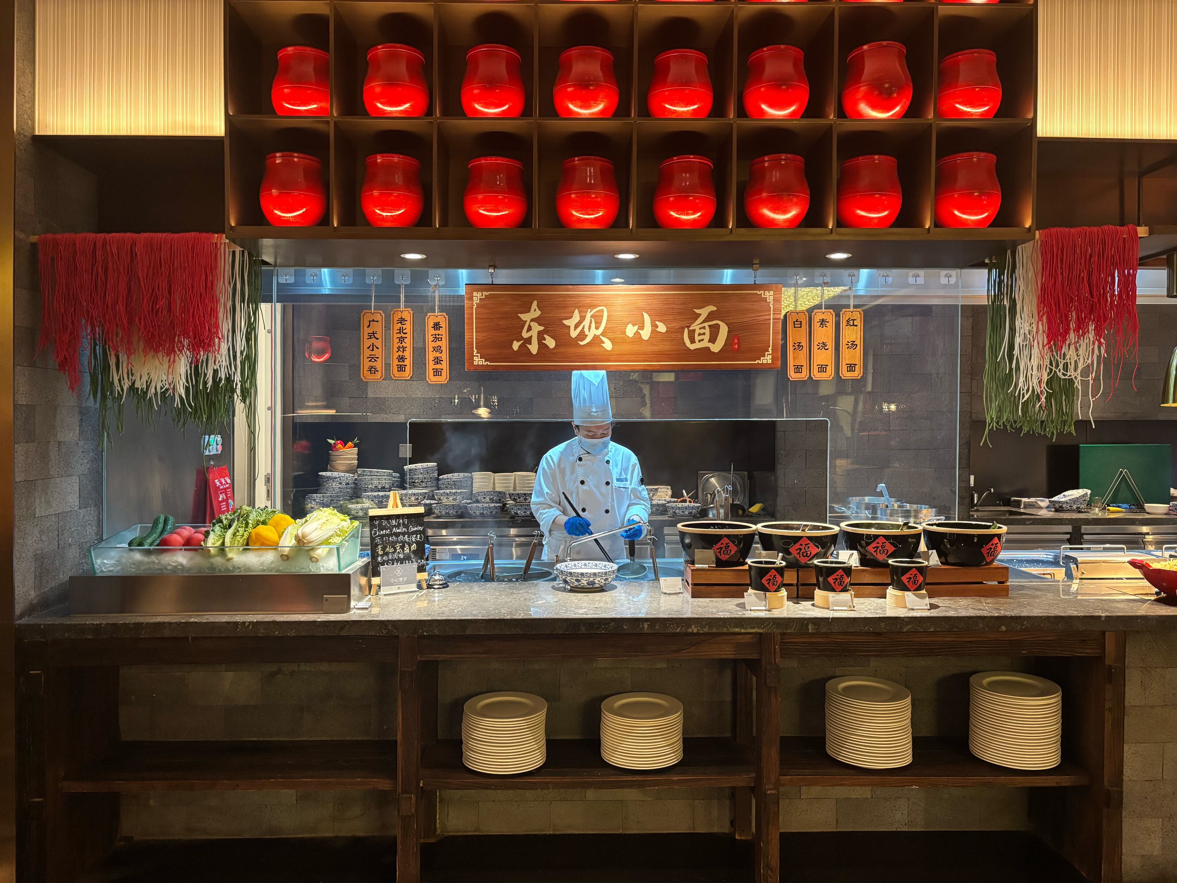 A restaurant with a chef preparing food, a display of red teapots, and a sign with Chinese characters.