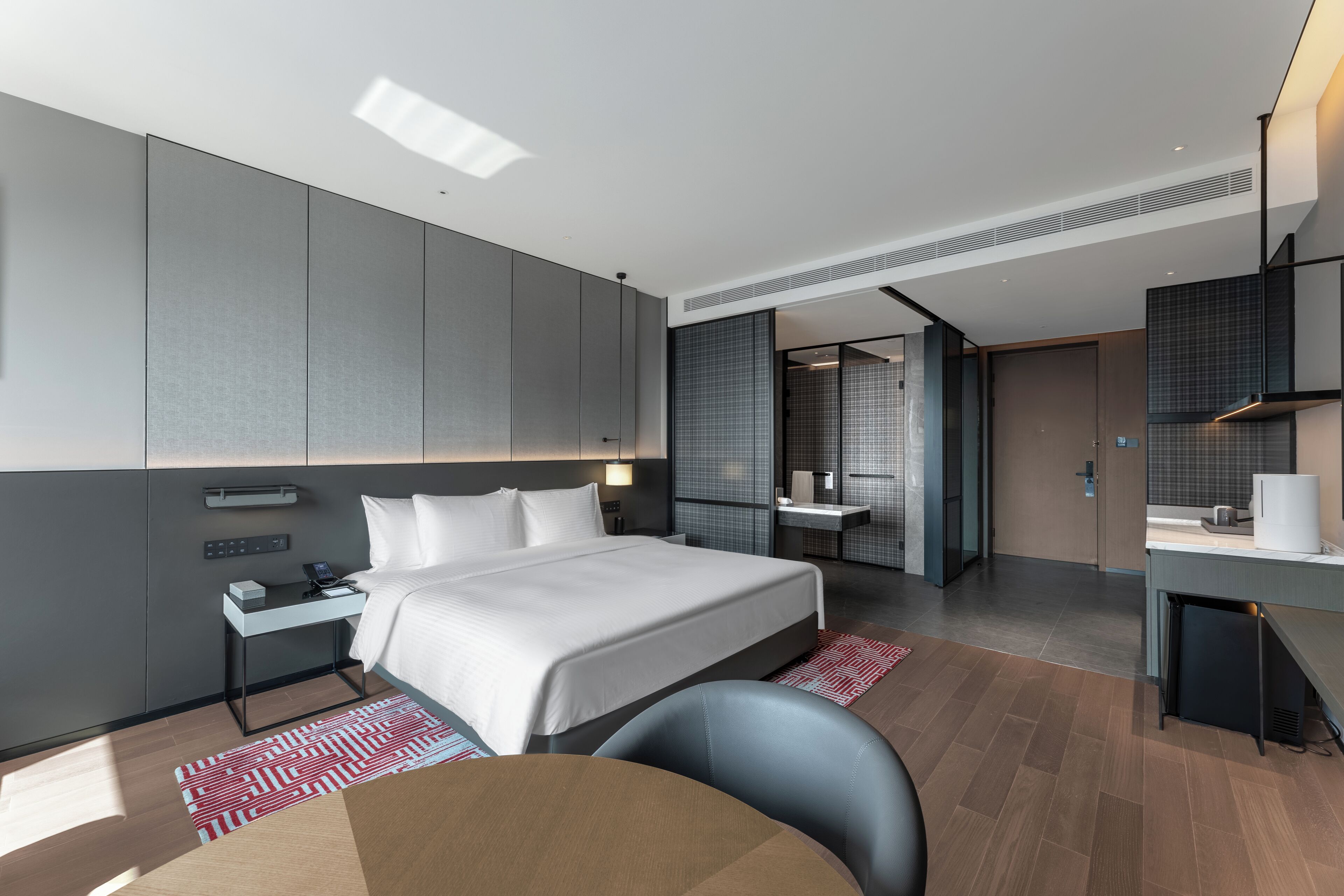 A modern hotel room with a large bed, a desk, and a separate bathroom area.