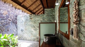 A bathroom with a stone wall, a large basin, and a wooden bench.