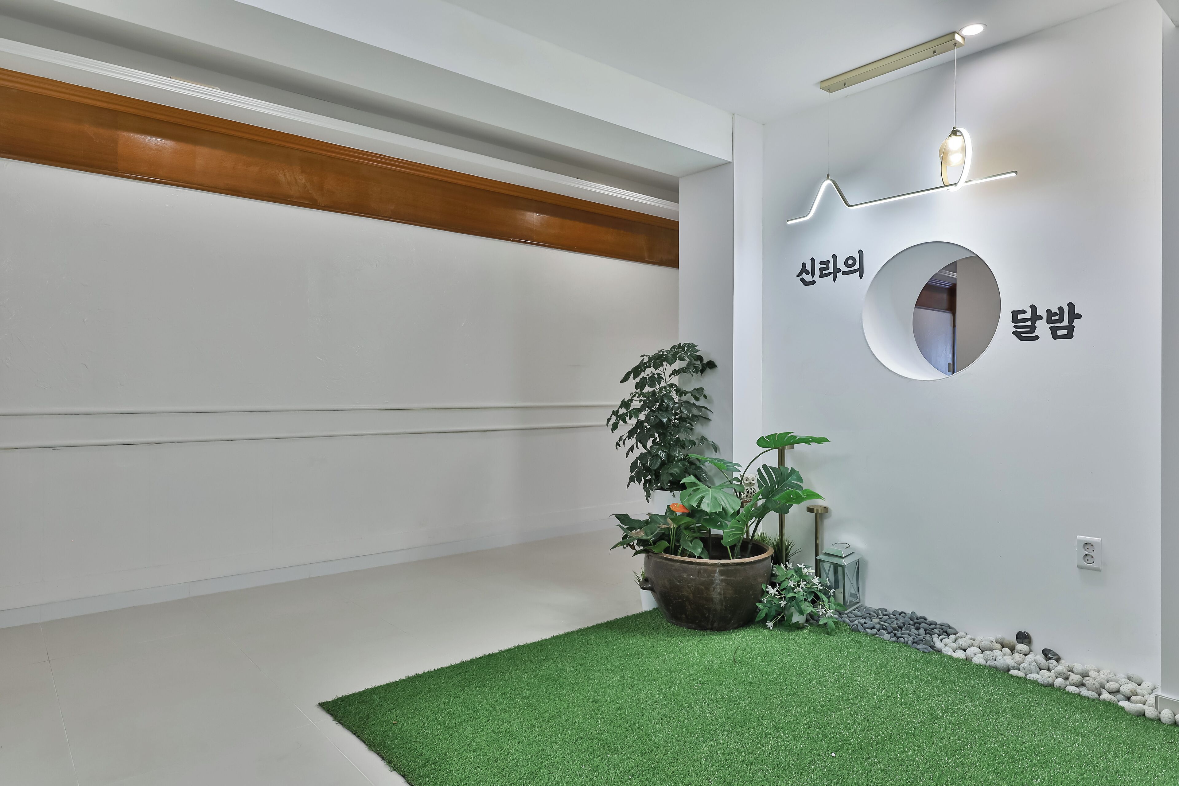Um interior moderno com teto de madeira, chão de grama sintética verde e espelho circular fixado na parede com texto coreano.