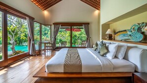 Ein geräumiges Schlafzimmer mit einem großen Bett, Holzboden, einer Decke mit Holzstruktur und Blick auf einen üppigen Garten und Pool durch große Fenster.