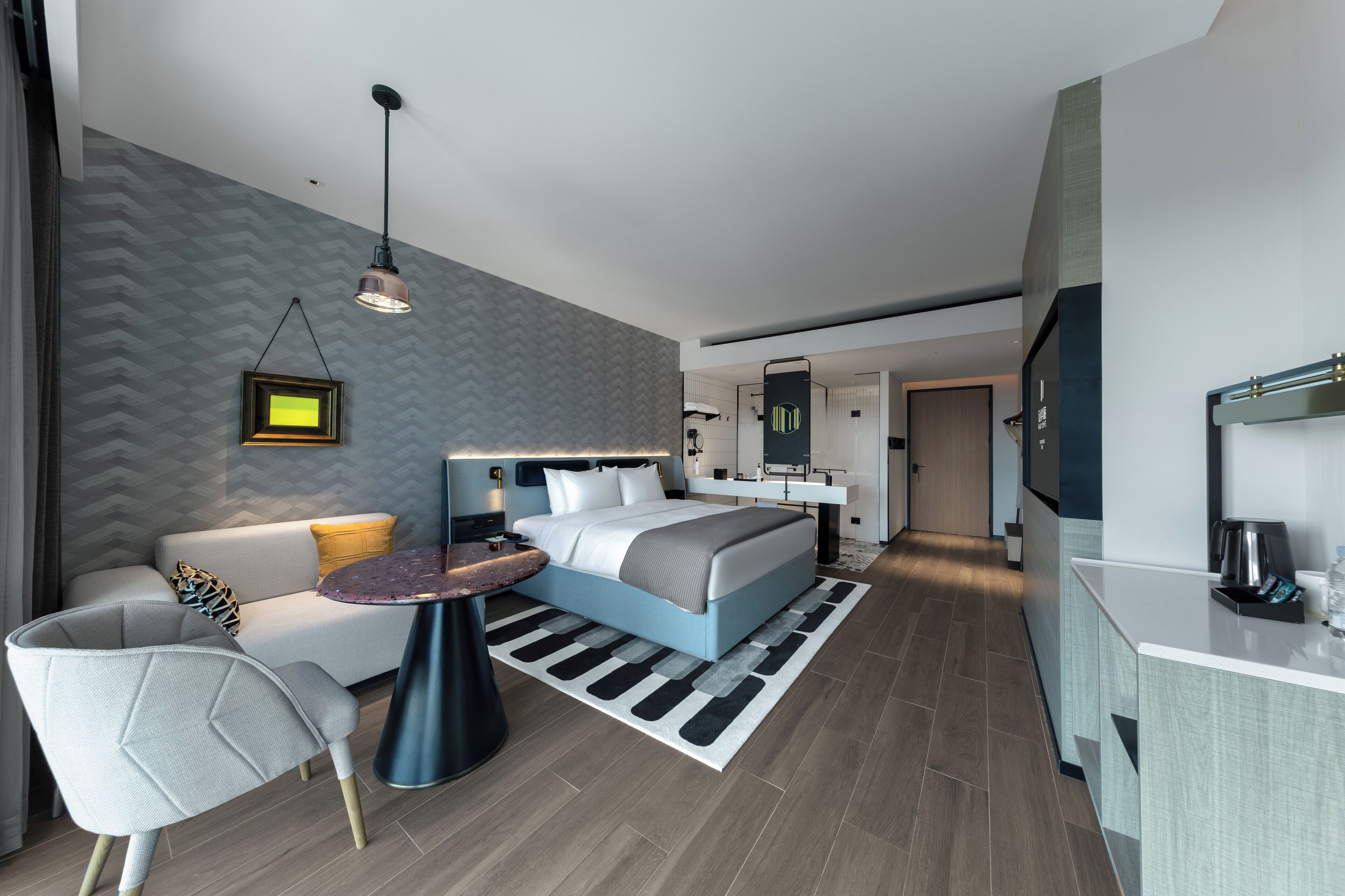 Een moderne hotelkamer met een bed, een bank, een tafeltje en een kitchenette.
