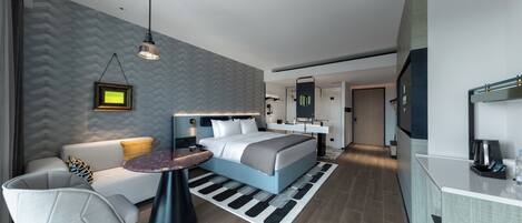 A modern hotel room with a bed, a sofa, a small table, and a kitchenette.