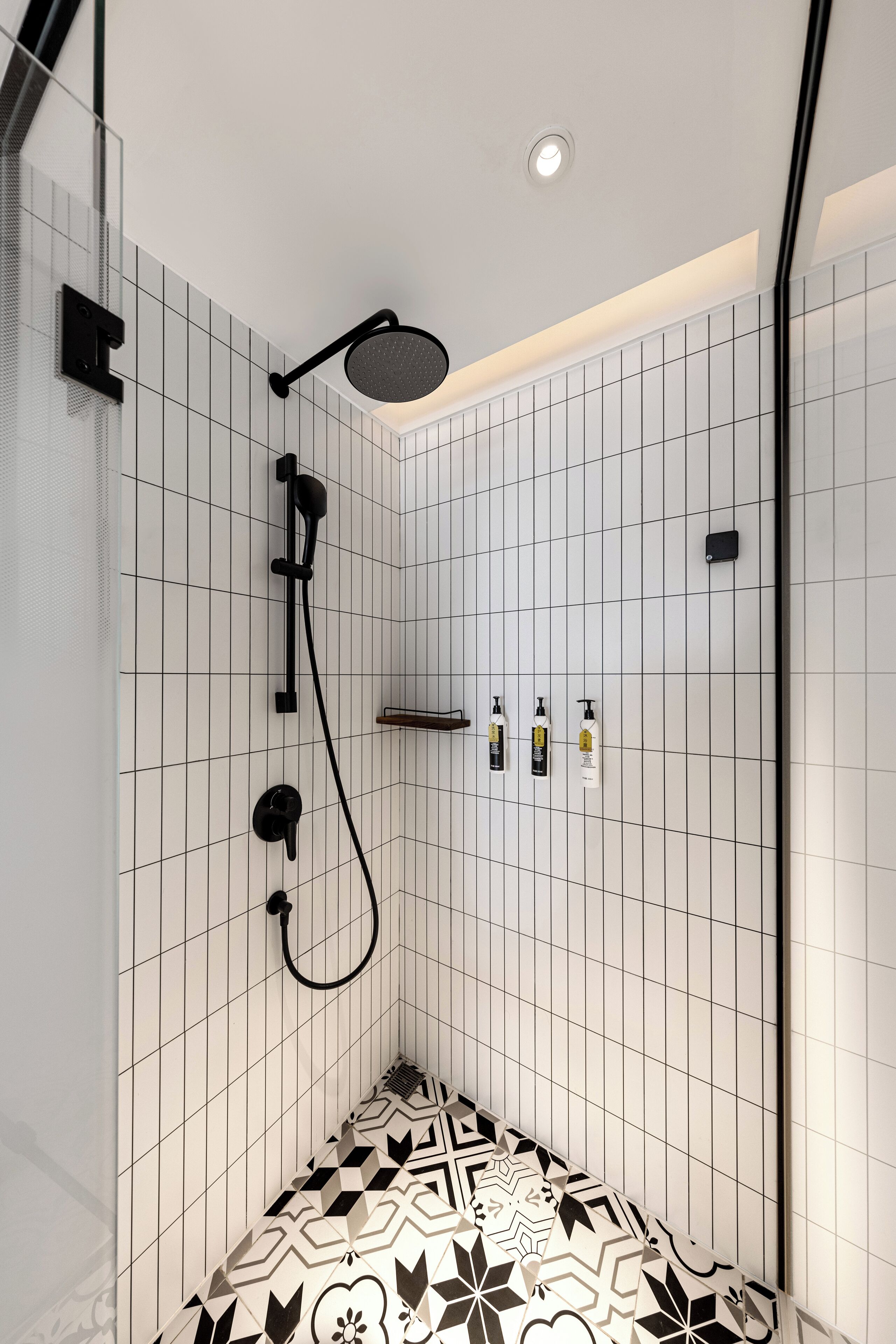 A modern shower area with a rain showerhead, handheld showerhead, and a handheld shower attachment. There are three bottles of shampoo and conditioner on a shelf.