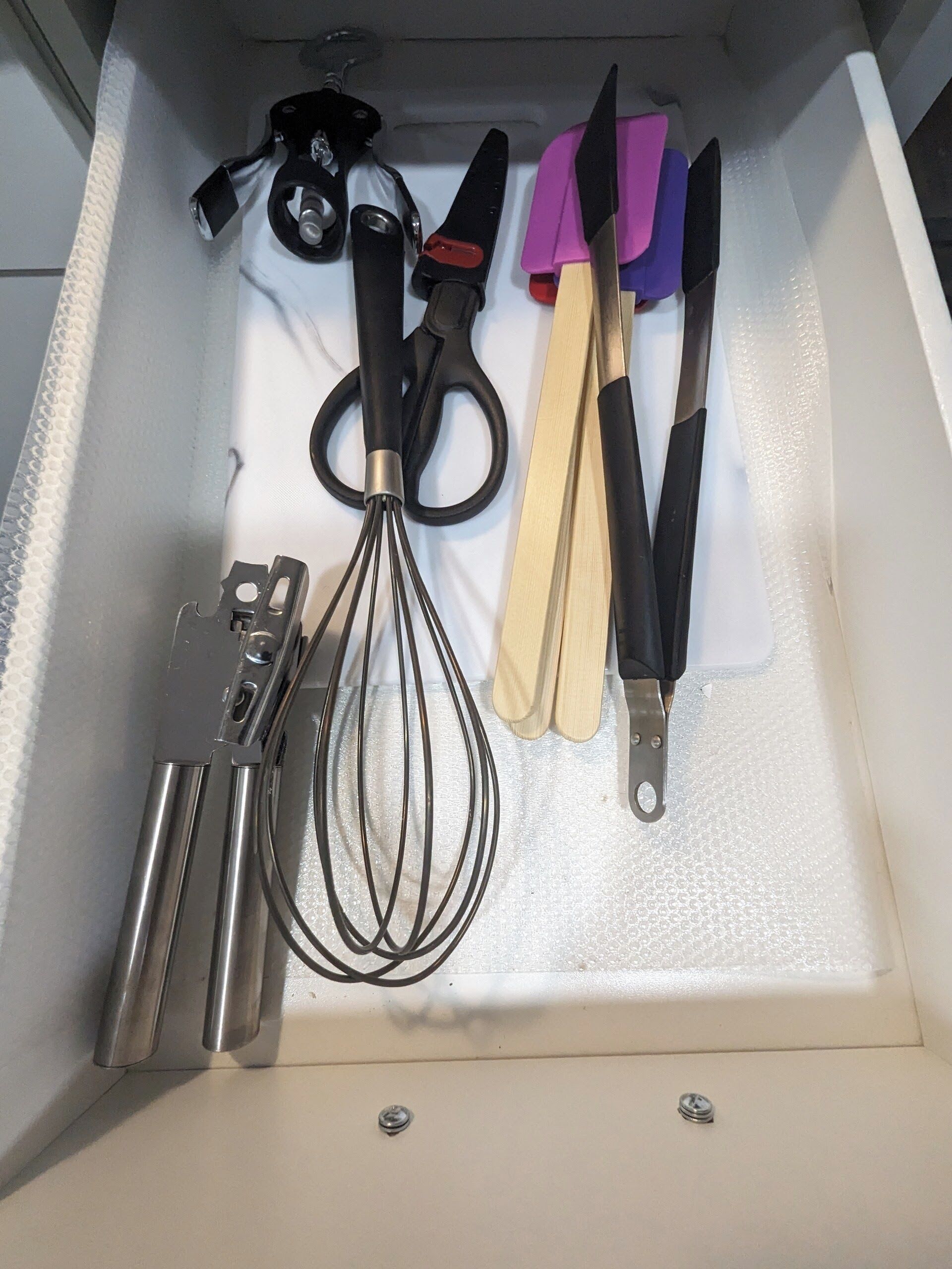 A drawer containing kitchen utensils including scissors, a whisk, and a knife.