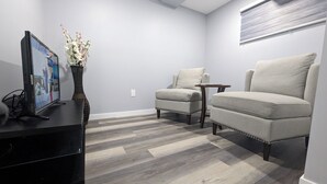 A modern living room with a flat-screen TV, a vase with flowers, two armchairs, and a small table.