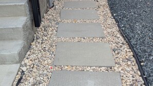 A pathway with stone slabs and pebbles leading to a wooden bench and a building entrance.