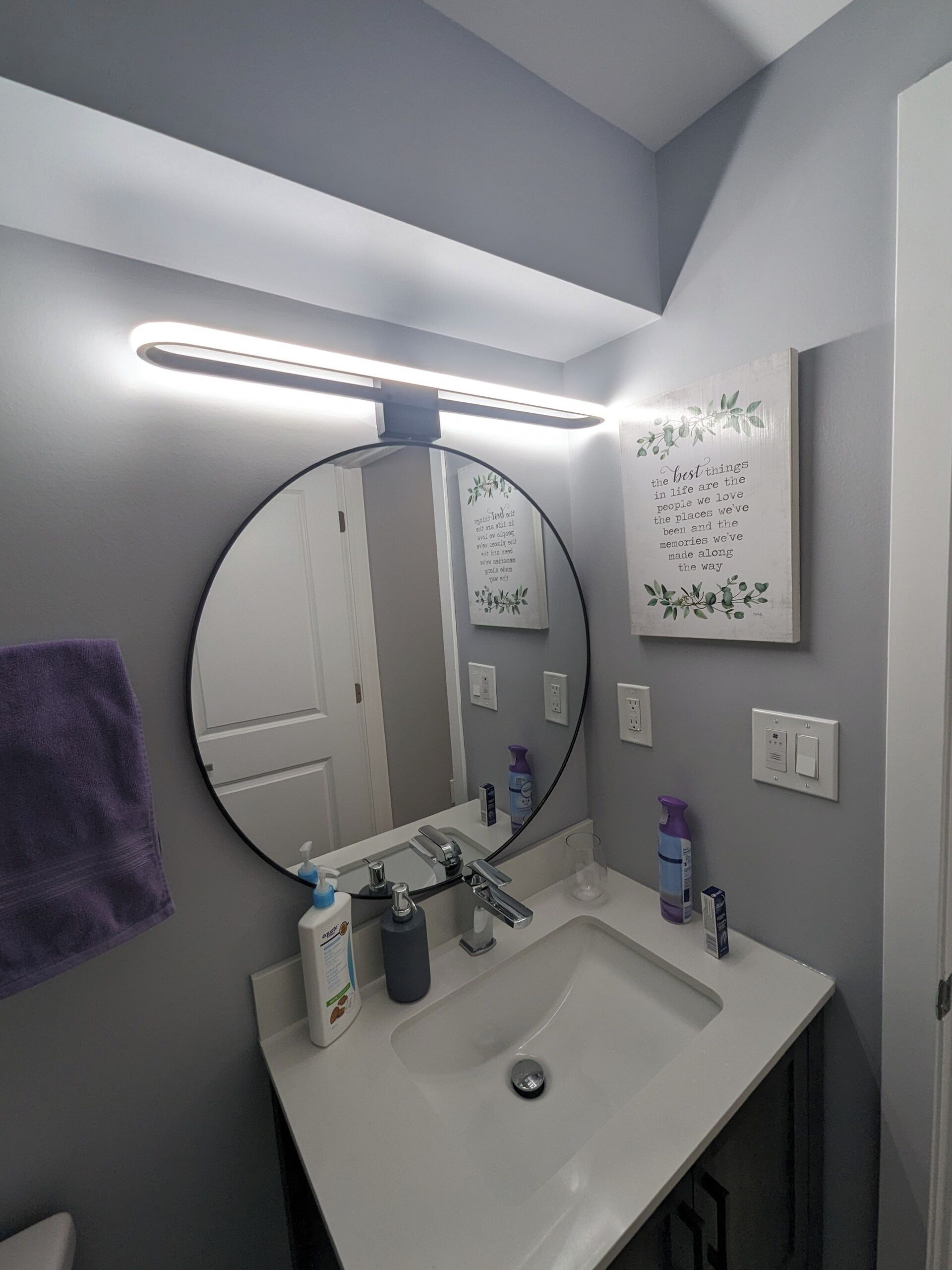 A bathroom with a round mirror, a white sink, and a purple towel.
