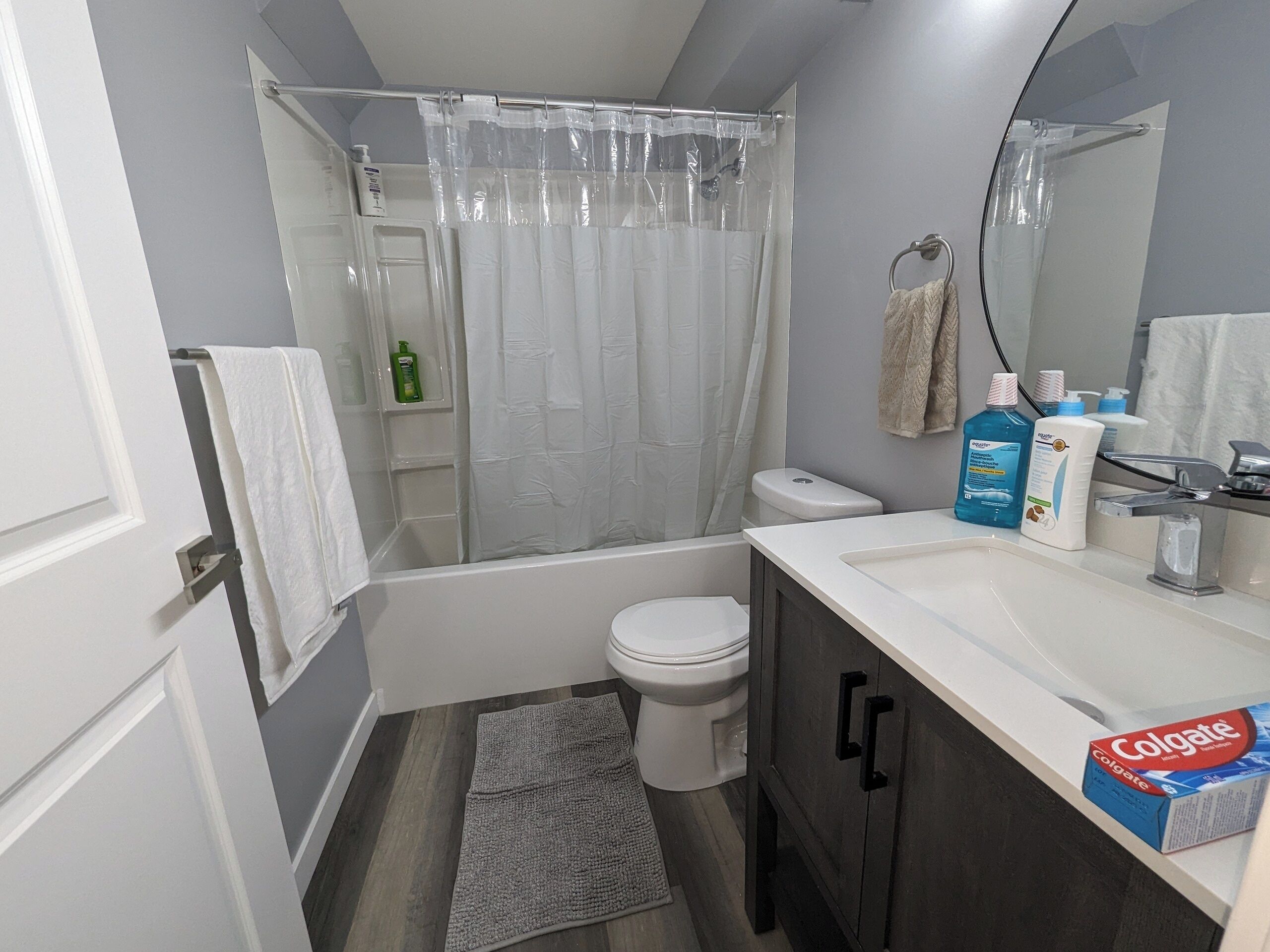A bathroom with a bathtub, toilet, and sink. There are toiletries on the sink and a shower curtain.