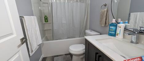 A bathroom with a bathtub, toilet, and sink. There are toiletries on the sink and a shower curtain.