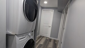 A laundry room with two stacked front-loading washing machines, a door, and a wooden floor.