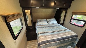 Ein kompaktes Schlafzimmer in einem Wohnmobil mit Bett, kleinem Fenster und Tür.