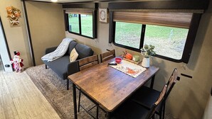 Ein kompaktes Wohnmobil-Interieur mit Essbereich, zwei Fenstern und einer kleinen Küchenzeile.