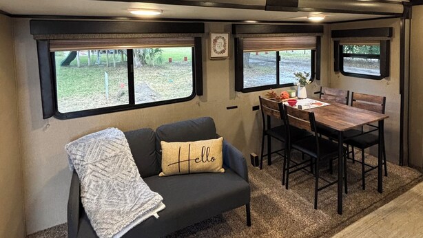 Ein kompaktes Wohnmobil-Interieur mit einer Sitzecke, einem Esstisch mit Stühlen und zwei Fenstern, die Blick auf eine Rasenfläche bieten.