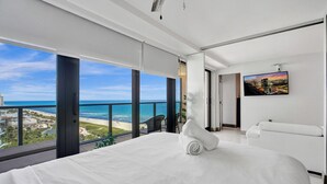 A modern hotel room with a large bed, a balcony with a view of the beach and ocean, and a cityscape painting on the wall. - Comfortable Beachside Condo with Pools & Gym Access 1404 (Miami Beach)