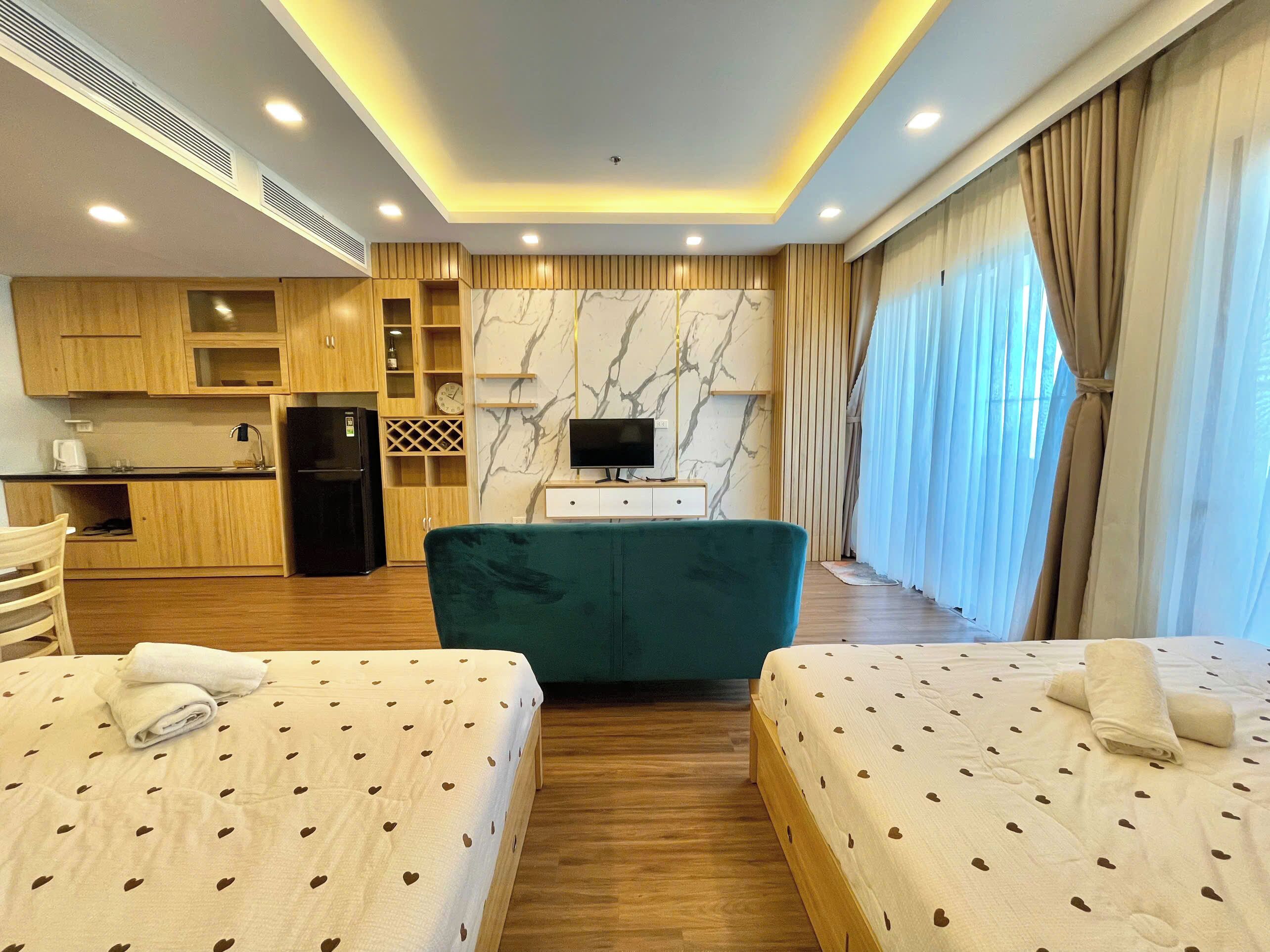 A hotel room with two beds, a kitchenette, a TV, and a marble wall.