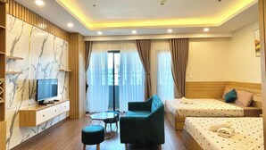 A modern hotel room with a flat-screen TV, a sofa, two single beds, a small table, and a glass-top coffee table. - Dan - FLC Sea Tower Quy Nhon (Quy Nhon Nam)